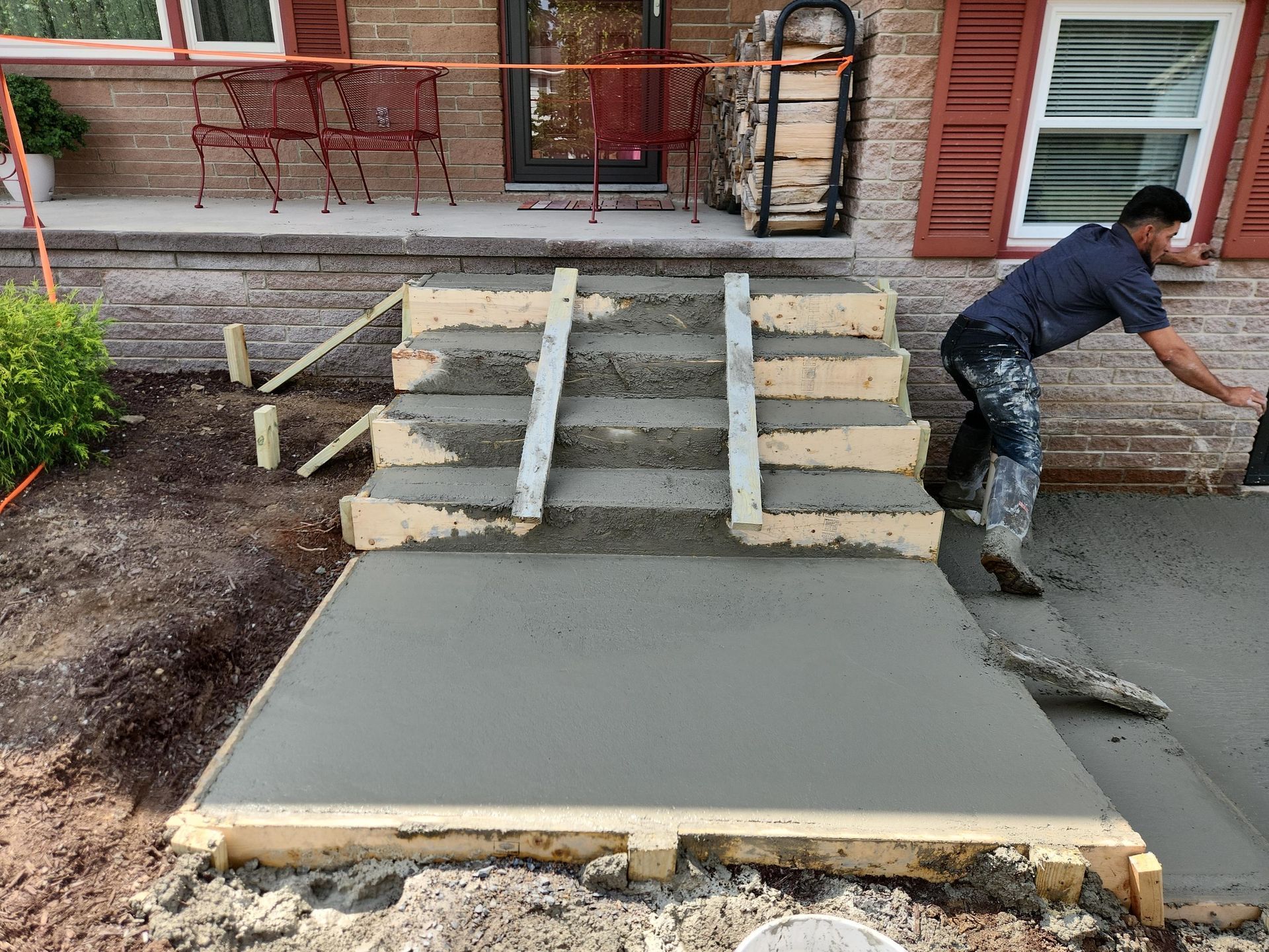 A person works on a newly poured concrete staircase and landing in front of a house, using metal forms to shape the steps.