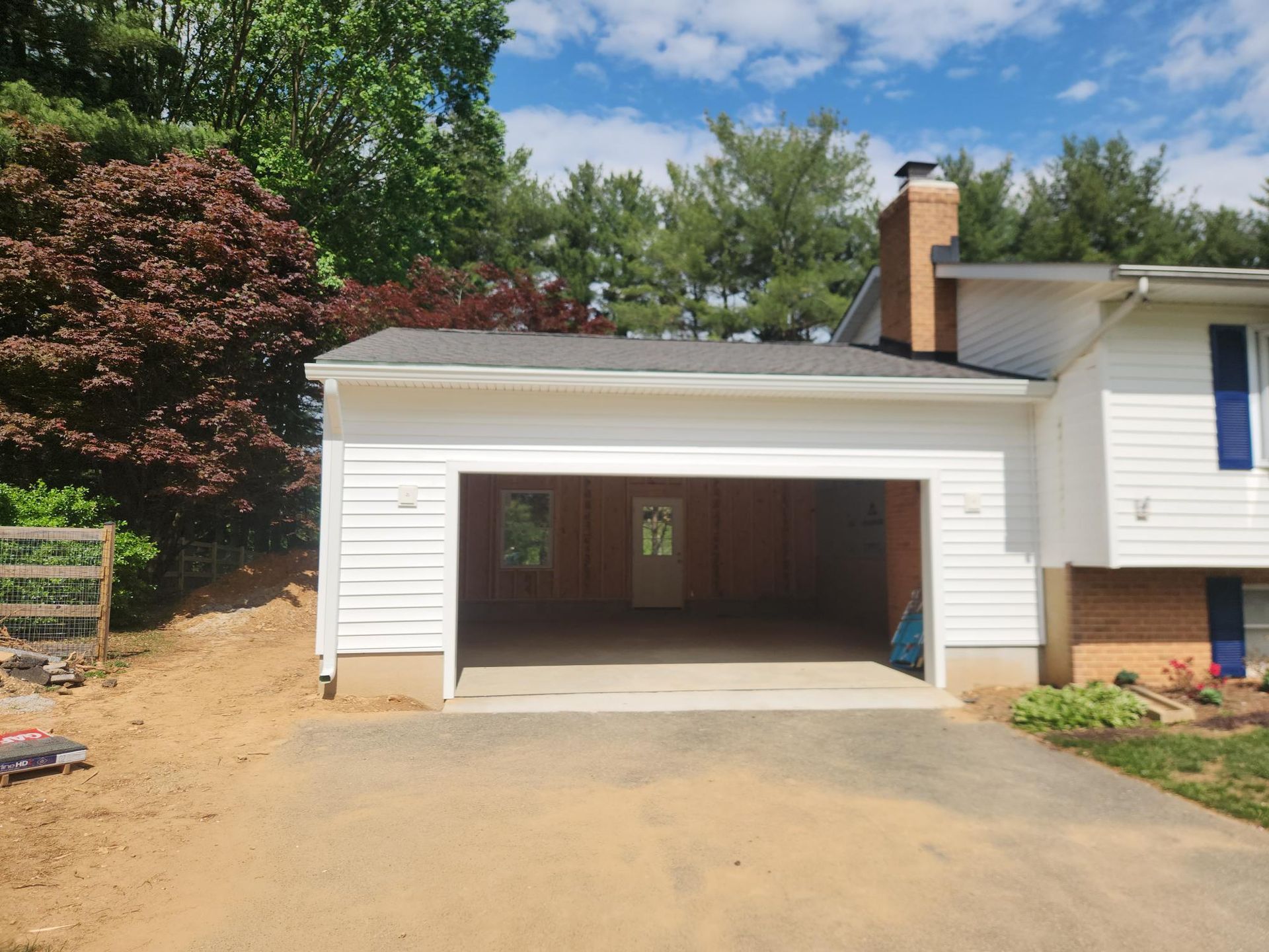 A white, single-story garage with an open door attached to a house with a brick chimney under a blue sky.