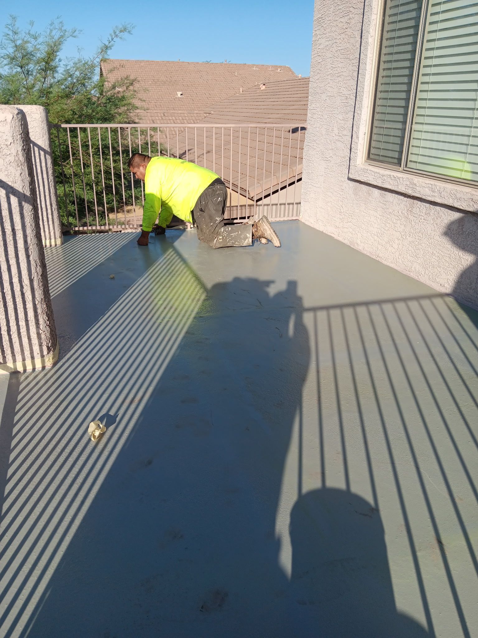 Worker in a neon shirt cleaning a sunny outdoor patio with a hose.