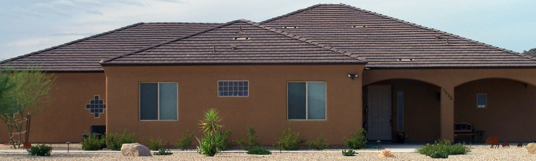 Single-story brick house with a brown tile roof, arched entryway, and desert landscaping