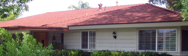 Single-story house with a red roof, white siding, and front windows surrounded by greenery.