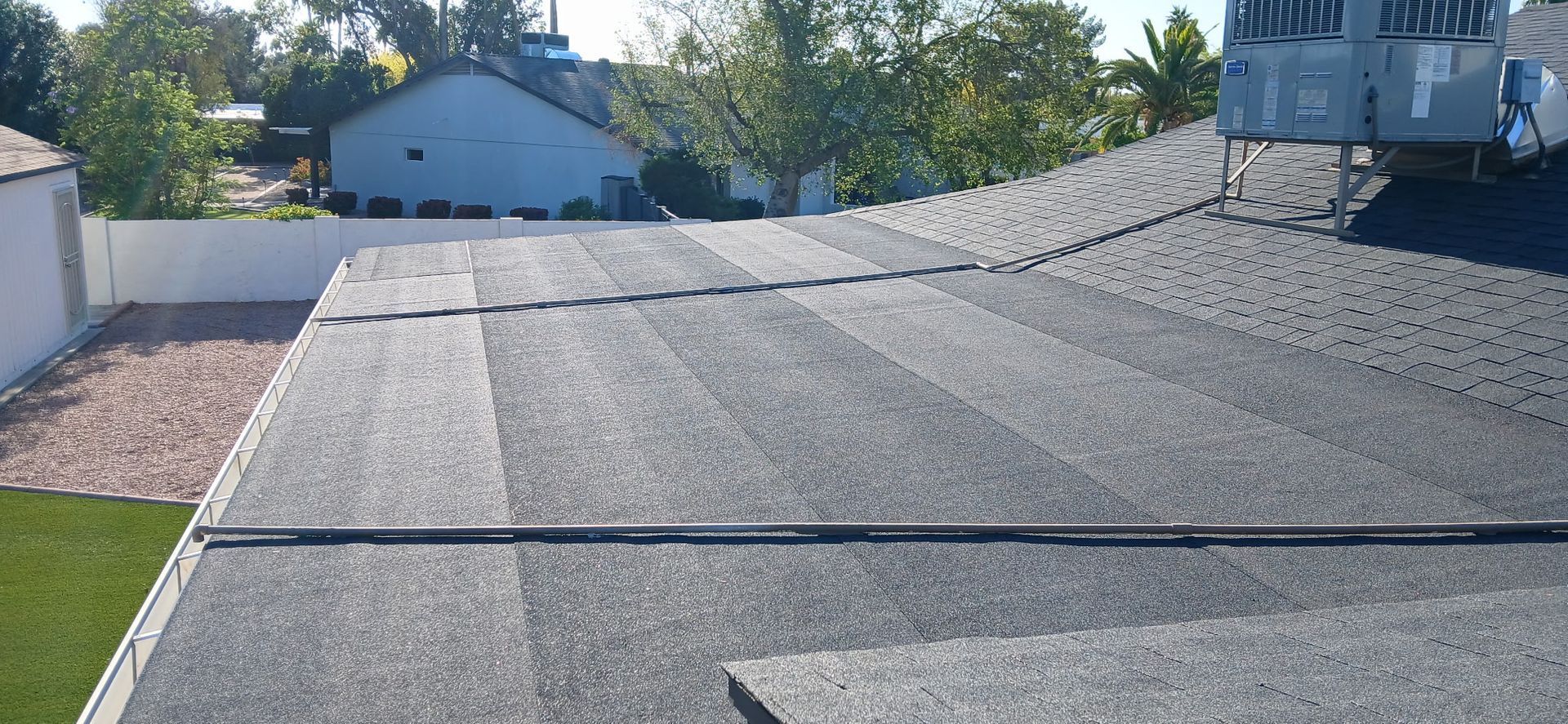 Flat gravel rooftop with a raised seam and a rooftop HVAC unit, viewed over a neighborhood in the background