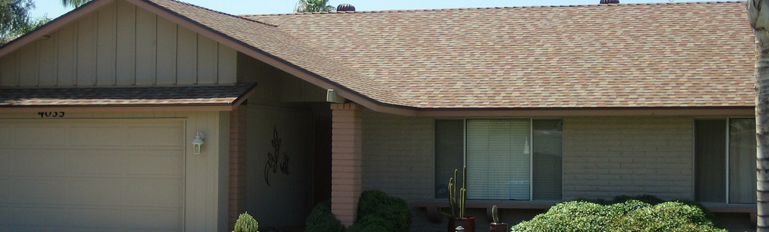 Single-story house with tan roof, beige siding, and a shaded front entry with shrubs.
