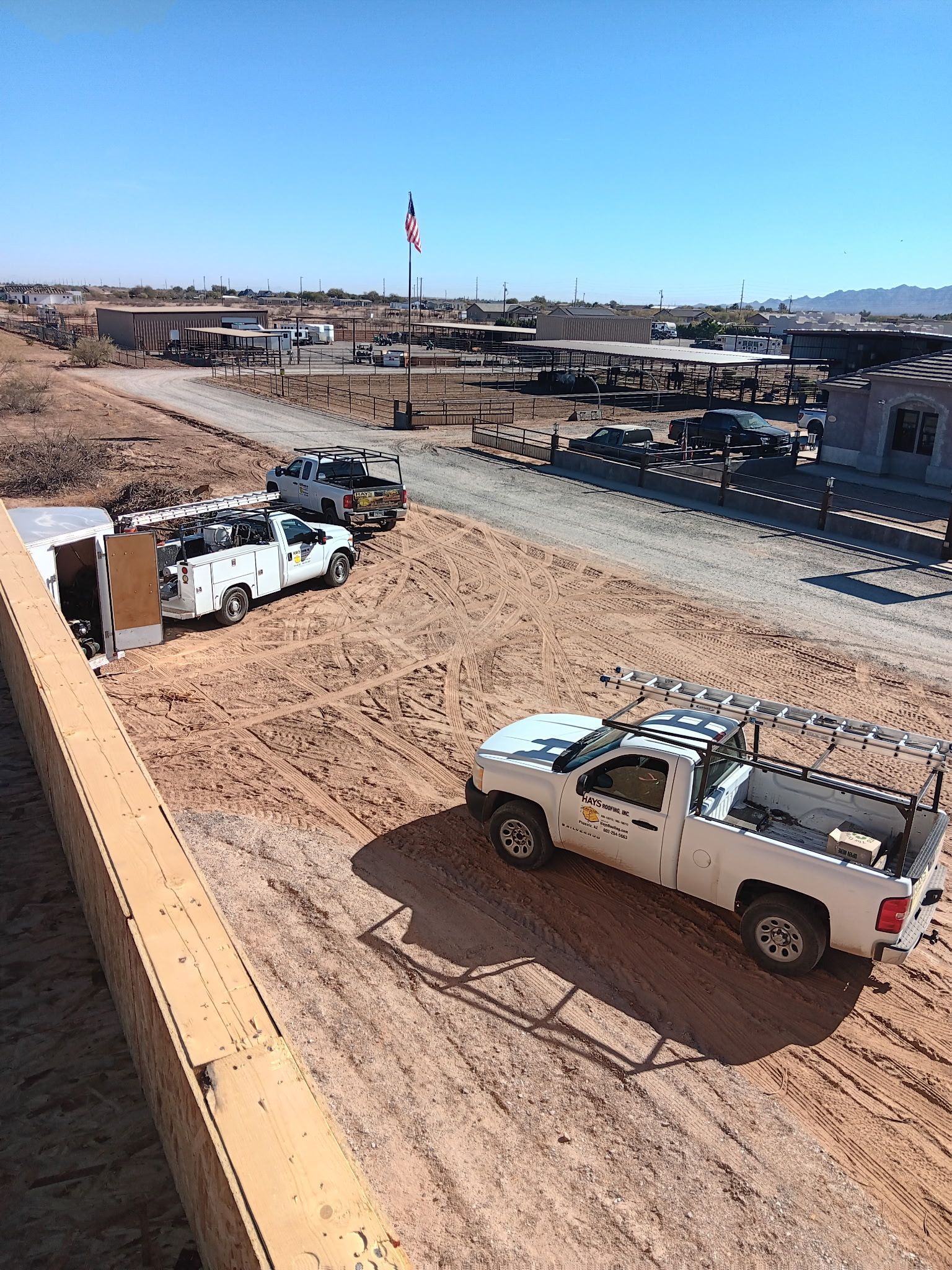White pickup trucks parked on a dusty construction site beside a paved road under a clear blue sky