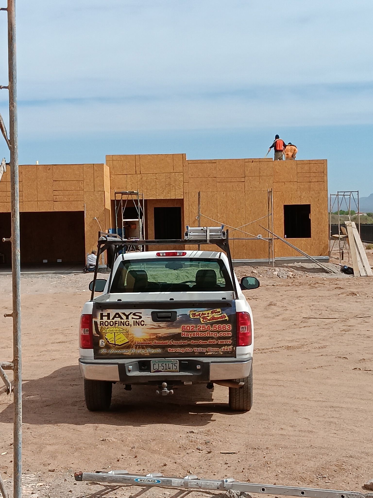 Pickup truck parked on a dirt lot in front of a partially built brick house under a blue sky