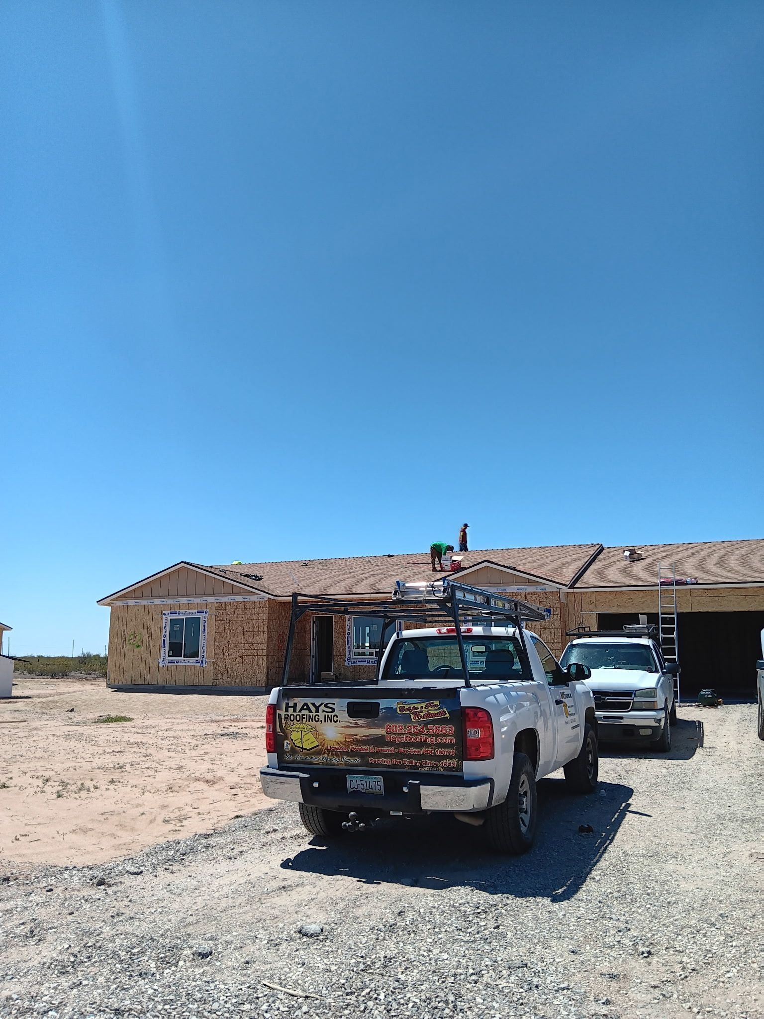 Two pickup trucks parked on a gravel lot beside a small brick house under a clear blue sky