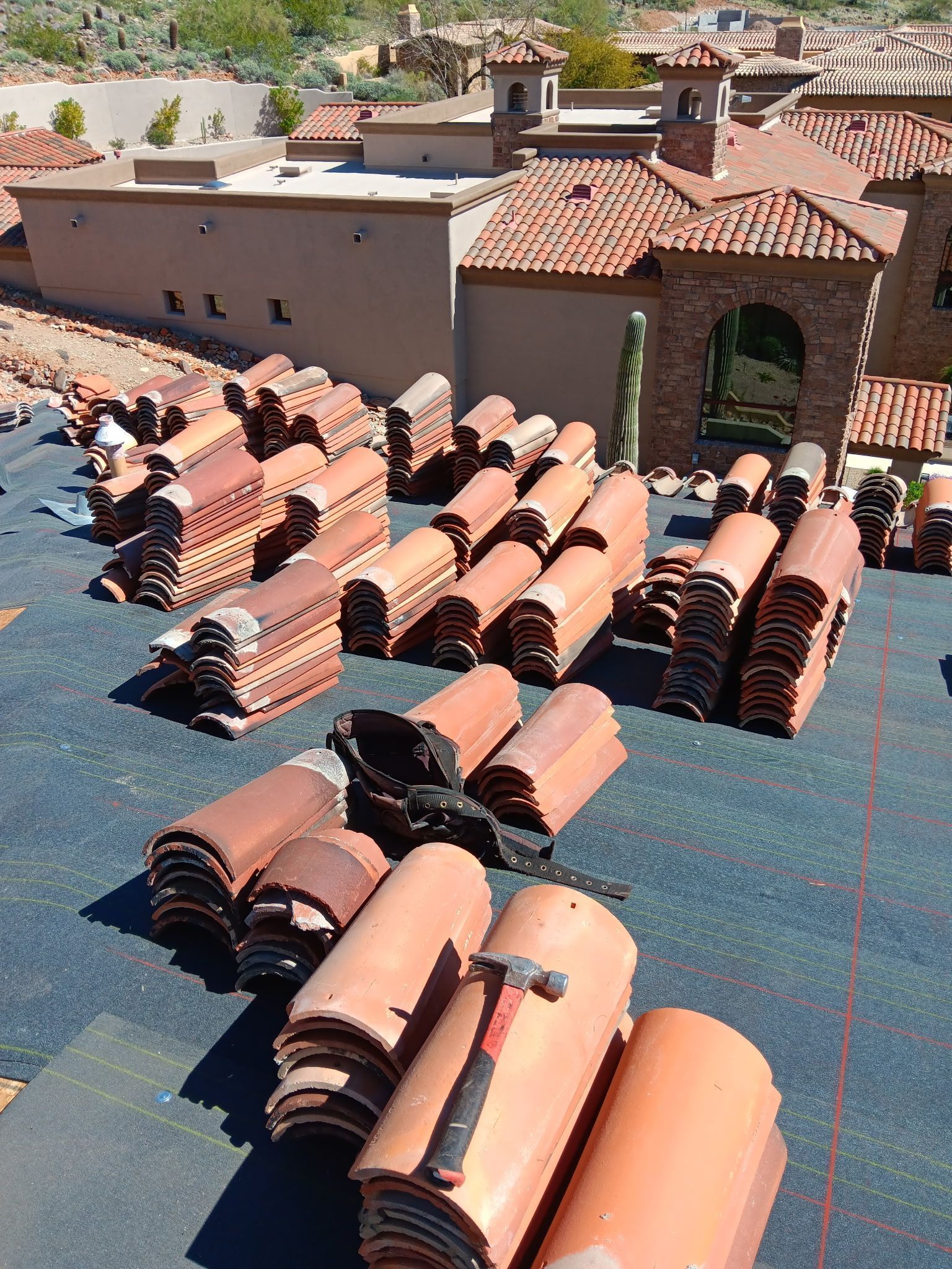 Stacks of terracotta roof tiles on a rooftop under bright sunlight, with a building in the background