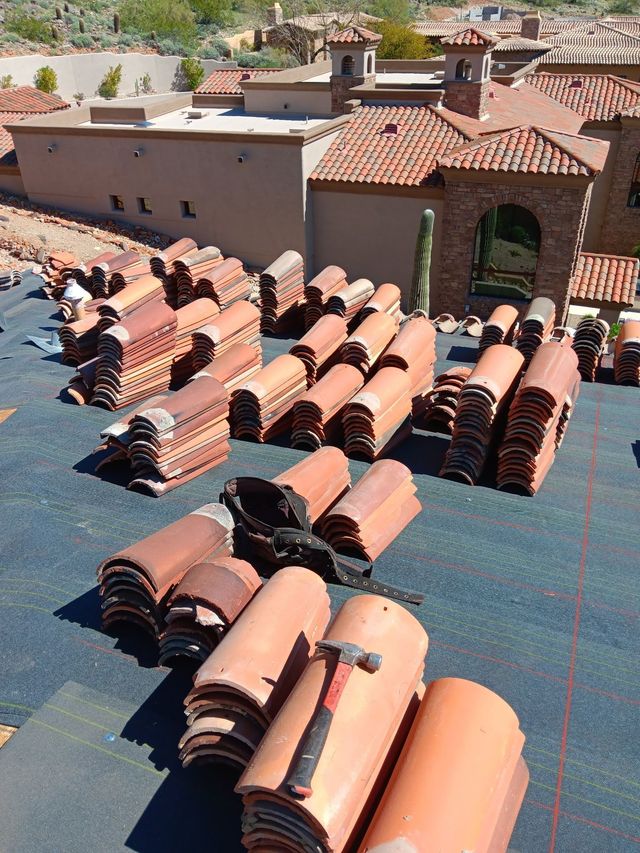 Stacks of terracotta roof tiles on a rooftop under bright sunlight, with a building in the background