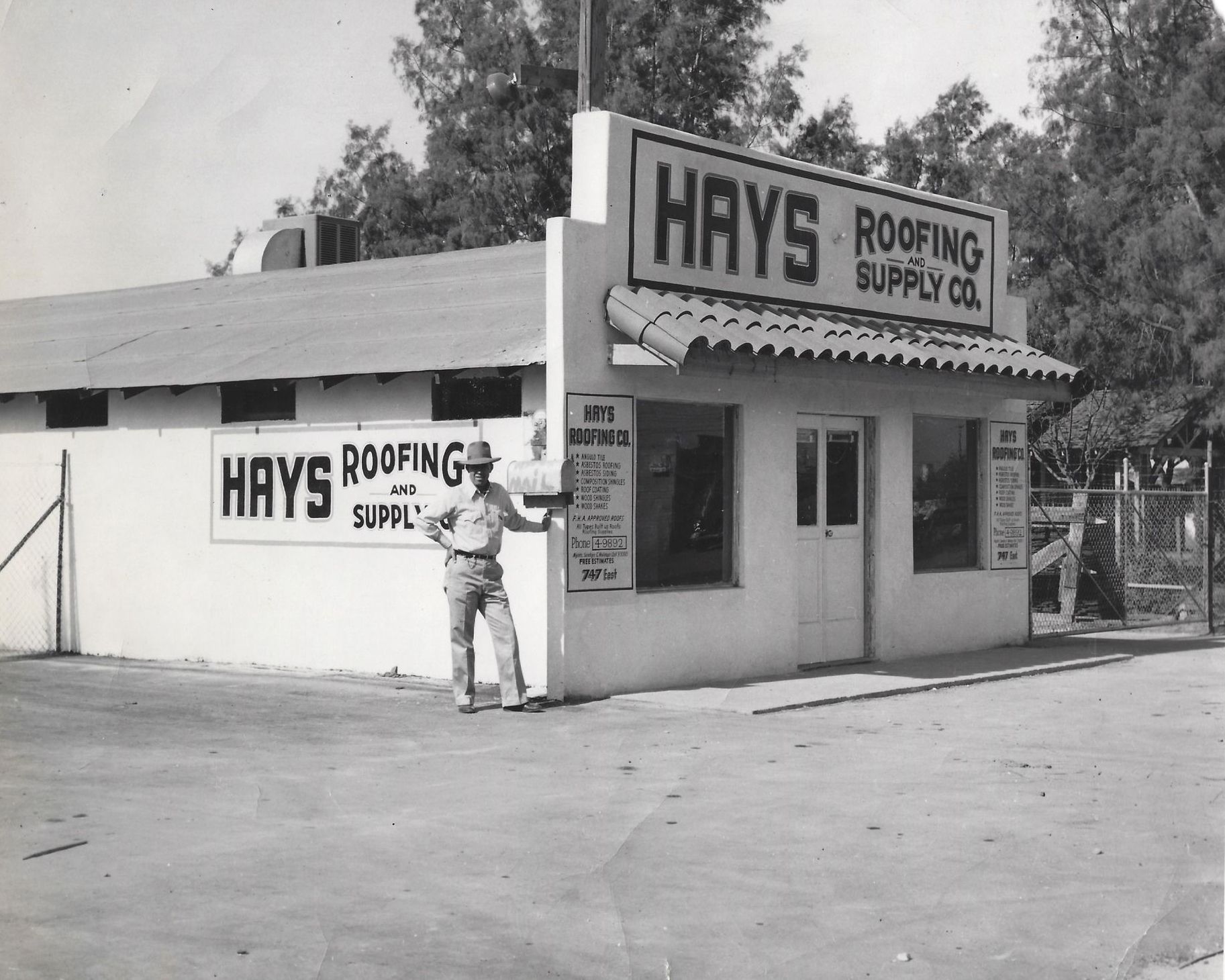 Man standing outside Hays Roofing Supply storefront with awning and signage, black-and-white scene