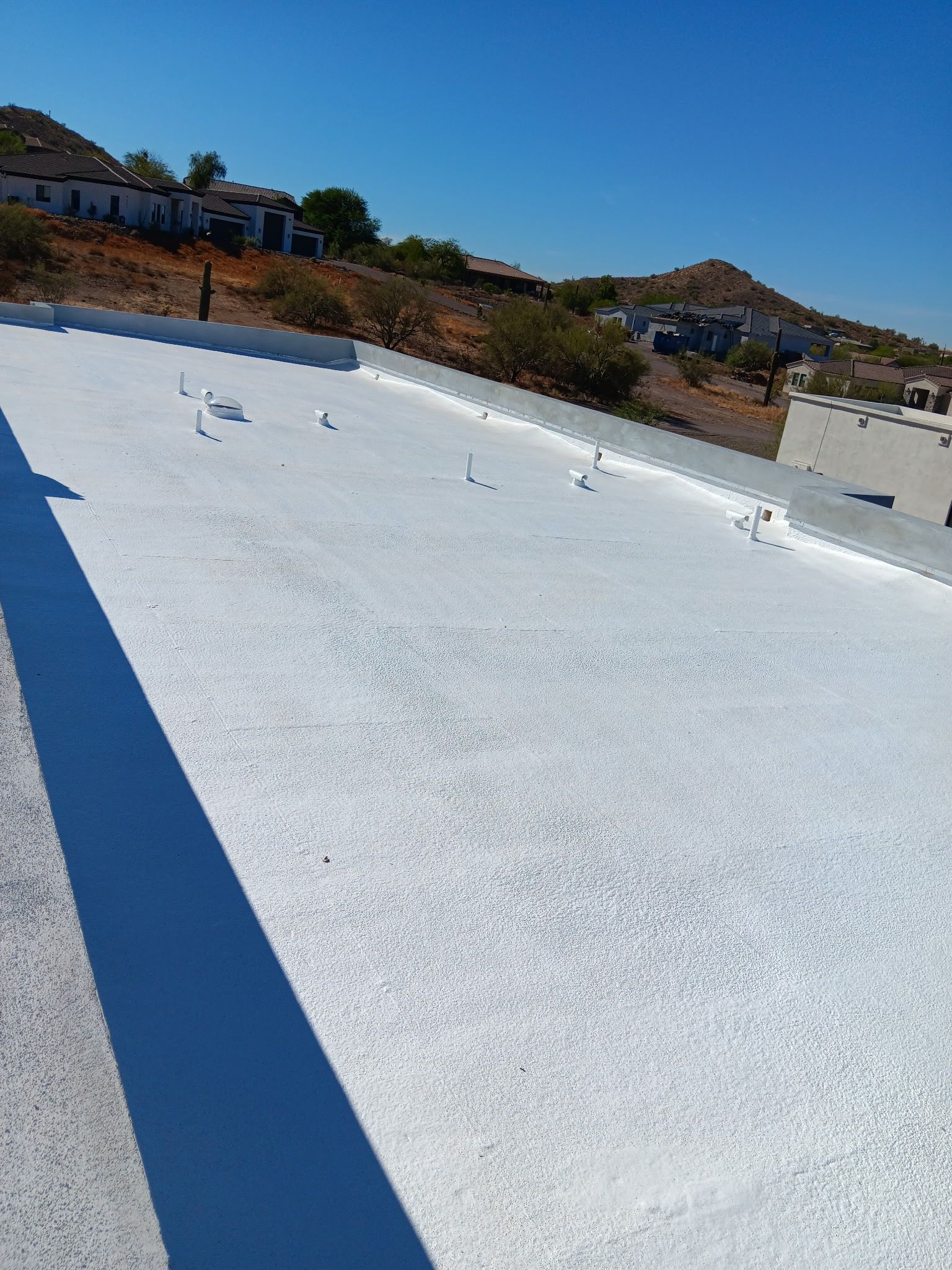 White rooftop or pool surface under bright sun, with buildings and hills in the background.
