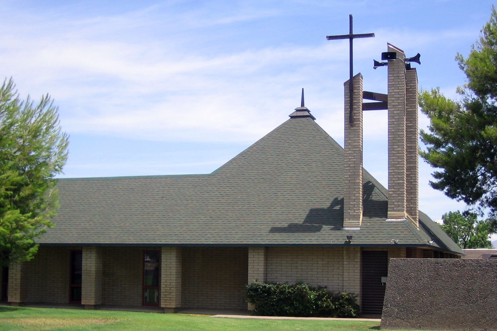 Small brick church with a green roof and cross-topped bell tower under a blue sky