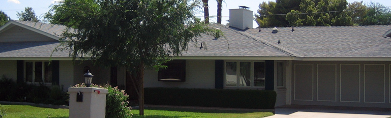 Single-story suburban house with a dark roof, front lawn, and garage under a sunny sky