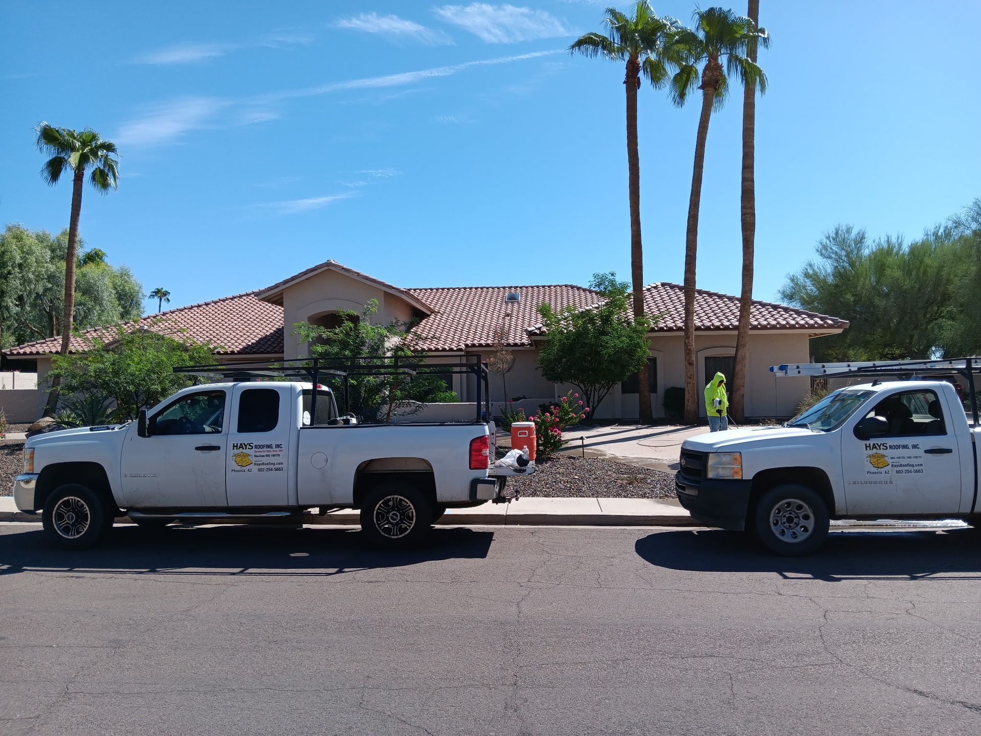 Two white pickup trucks parked in front of a single-story house with palm trees and workers nearby