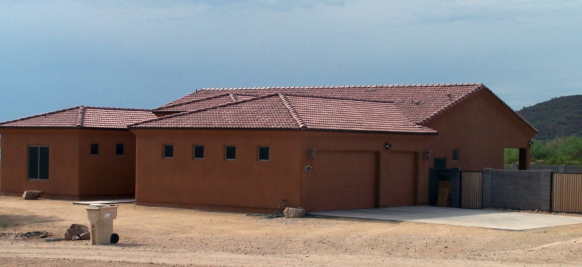 Single-story red-brick building with a corrugated roof and garage doors in a dusty rural area.