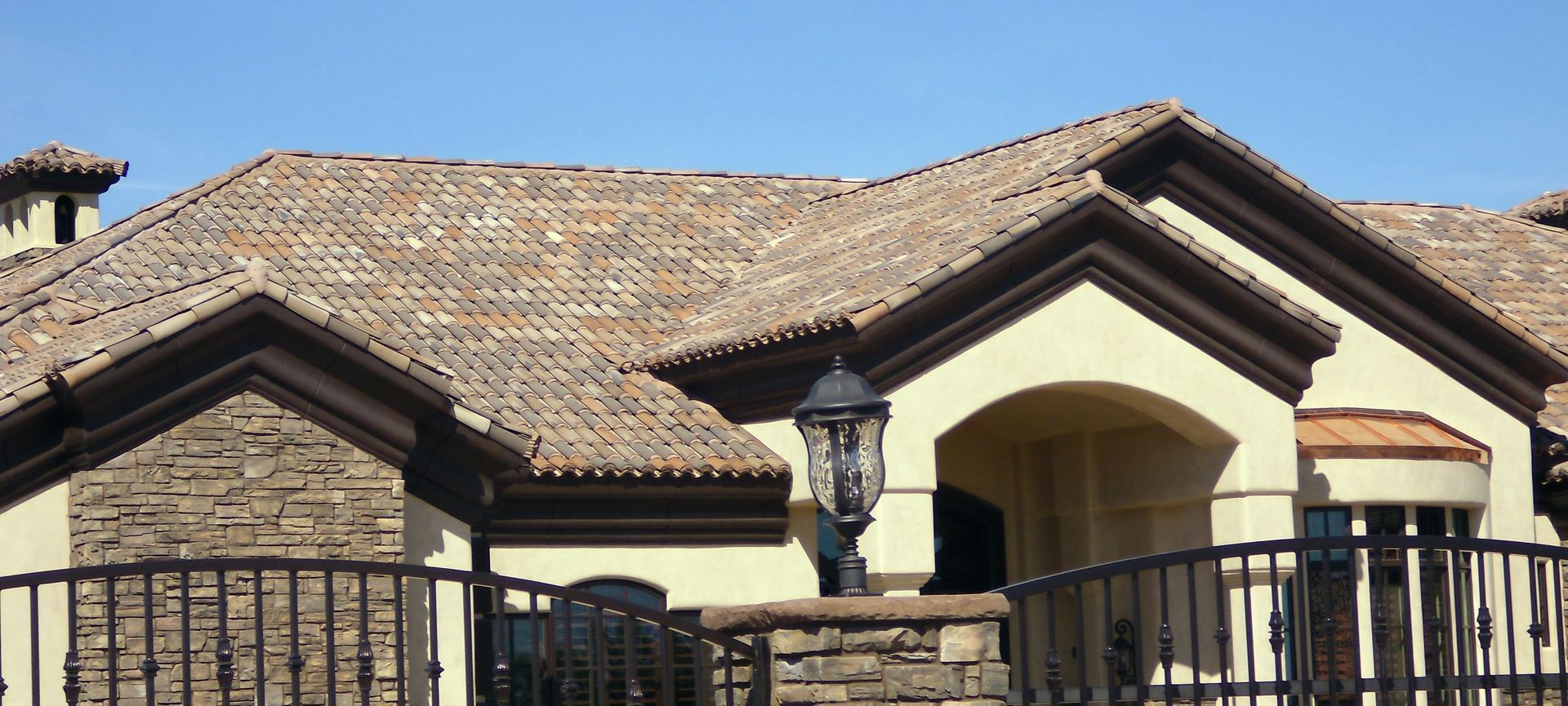 Suburban house with a tiled roof and stone facade behind a black metal fence