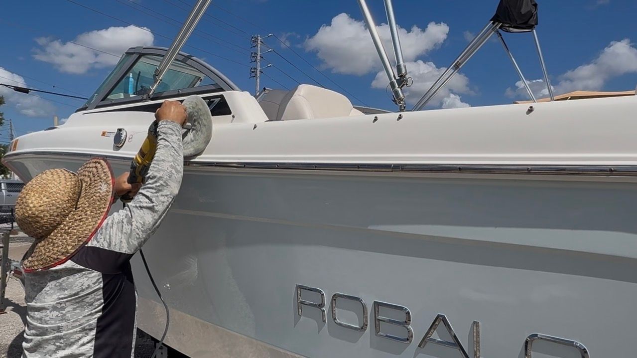 Person in a straw hat working on a white sailboat under a blue sky