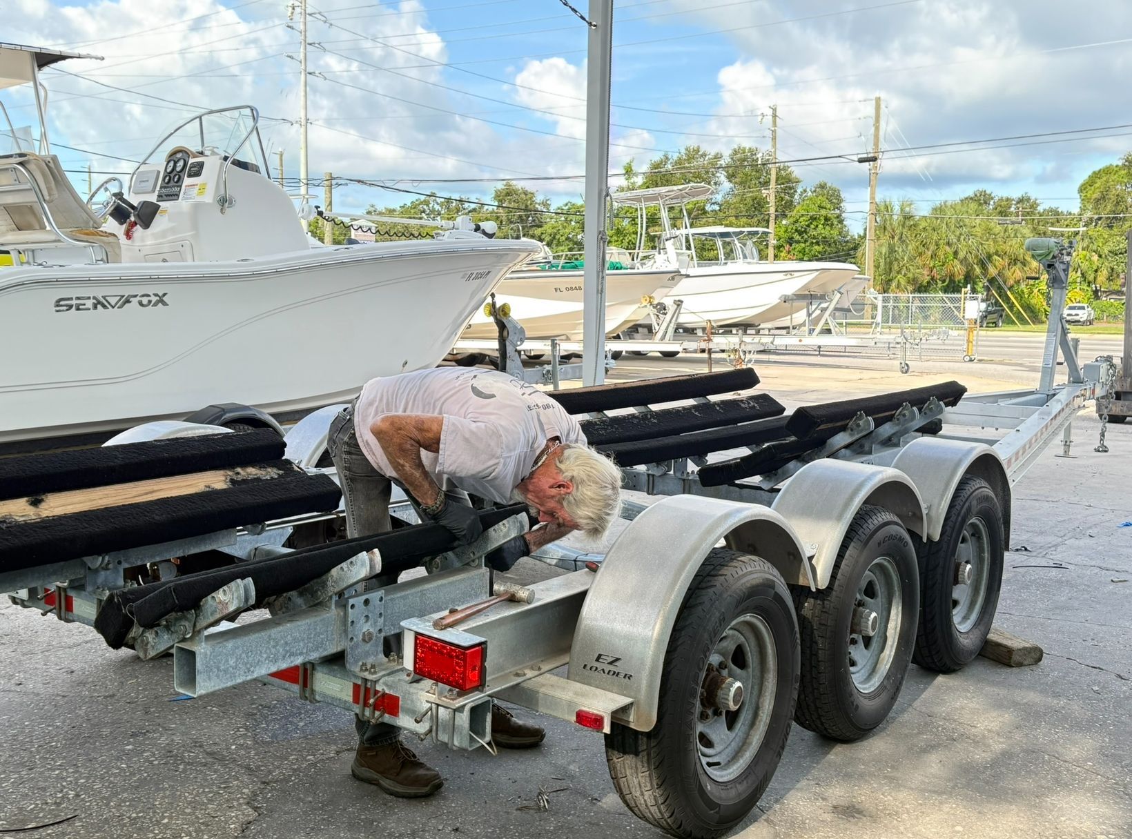 Person loading a white boat onto a black trailer at a marina