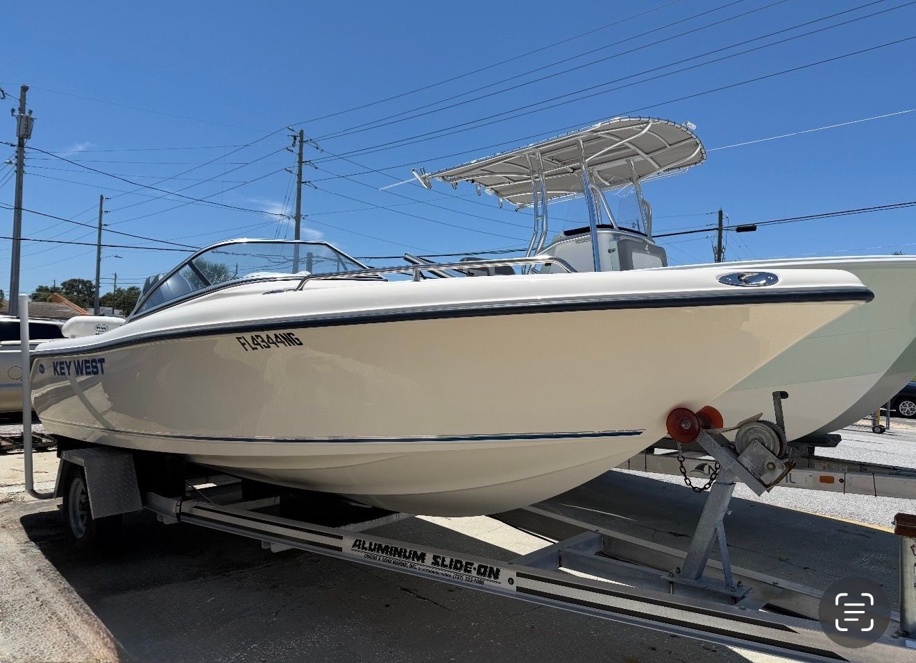 White center-console boat on a trailer at a marina under a clear blue sky