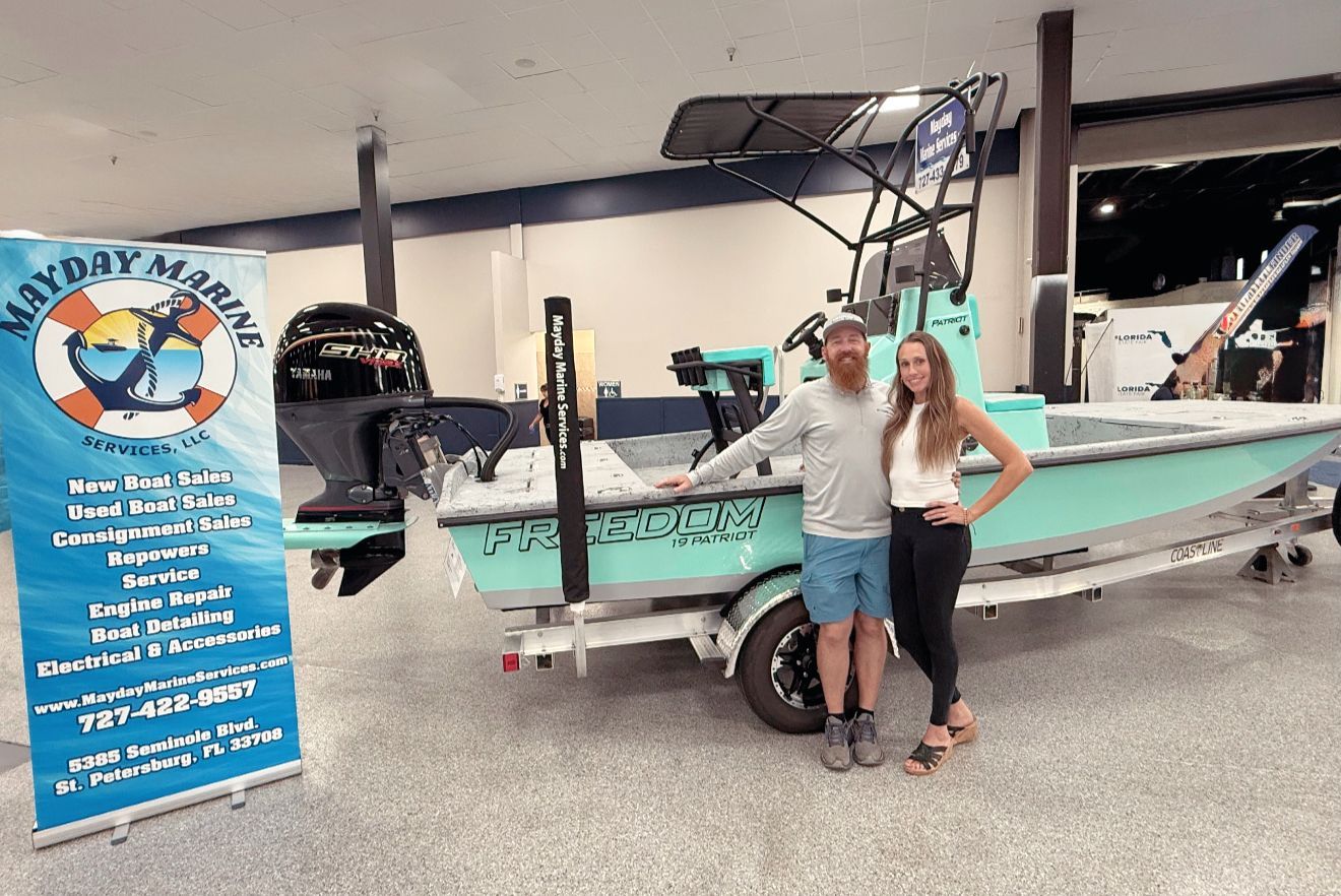 Two people standing beside a teal boat on a trailer in a showroom, with a blue sign nearby