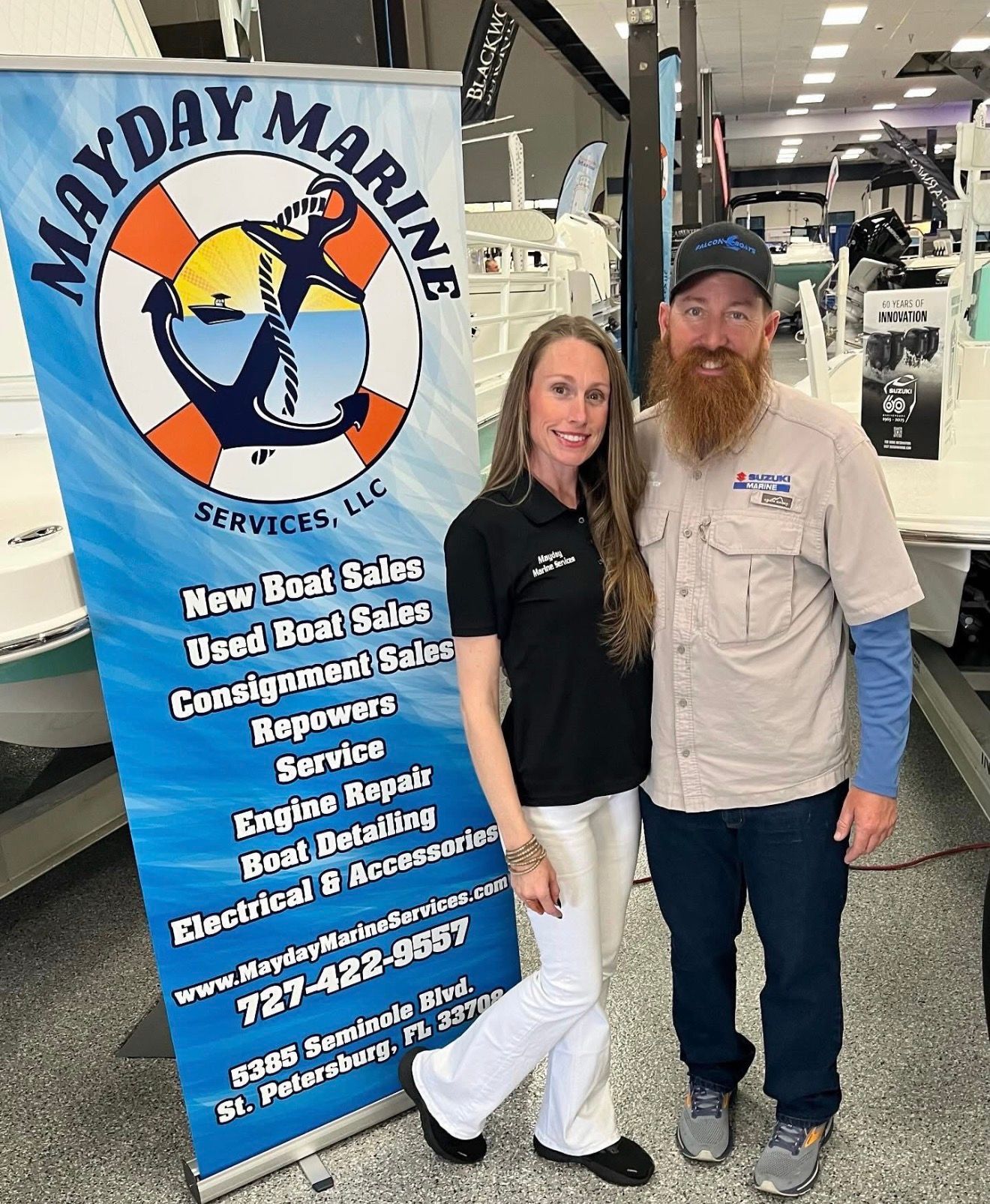 Two people posing beside a “Mayday Marine” service banner inside a marine store.