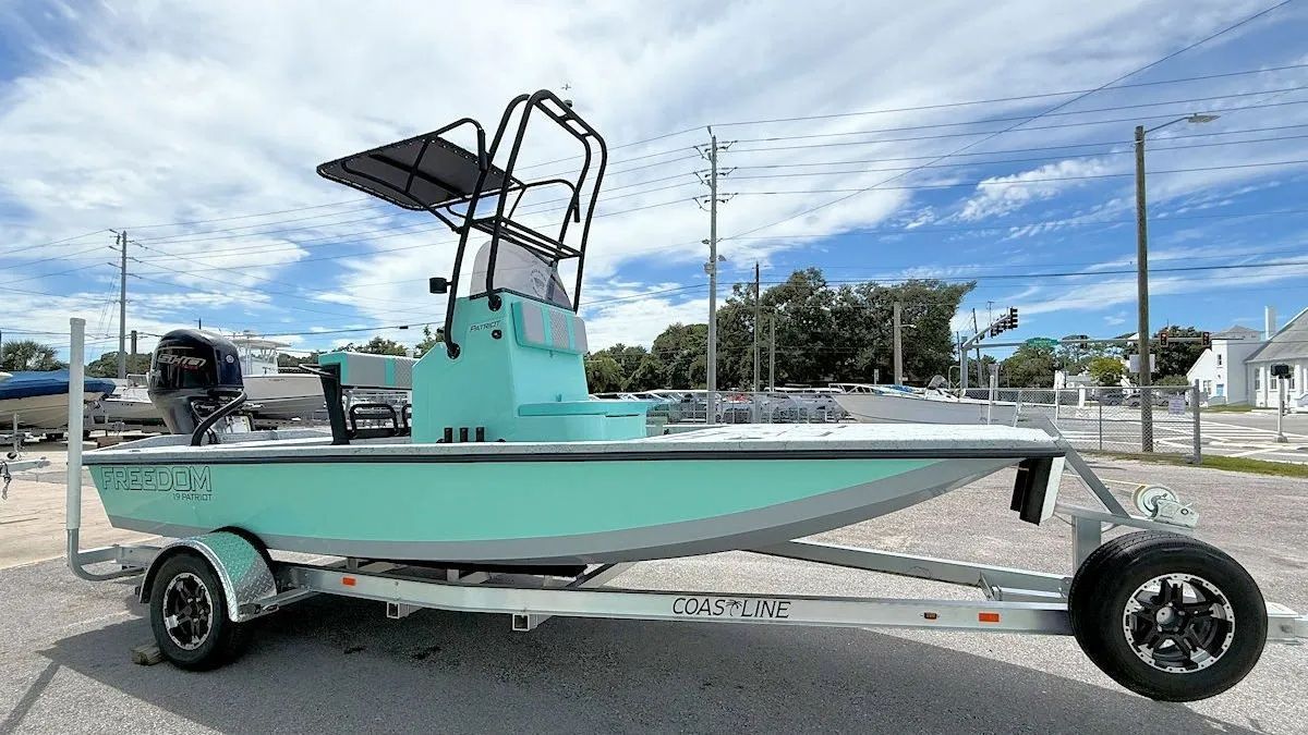 Mint green fishing boat on a trailer at a boat ramp under a partly cloudy sky