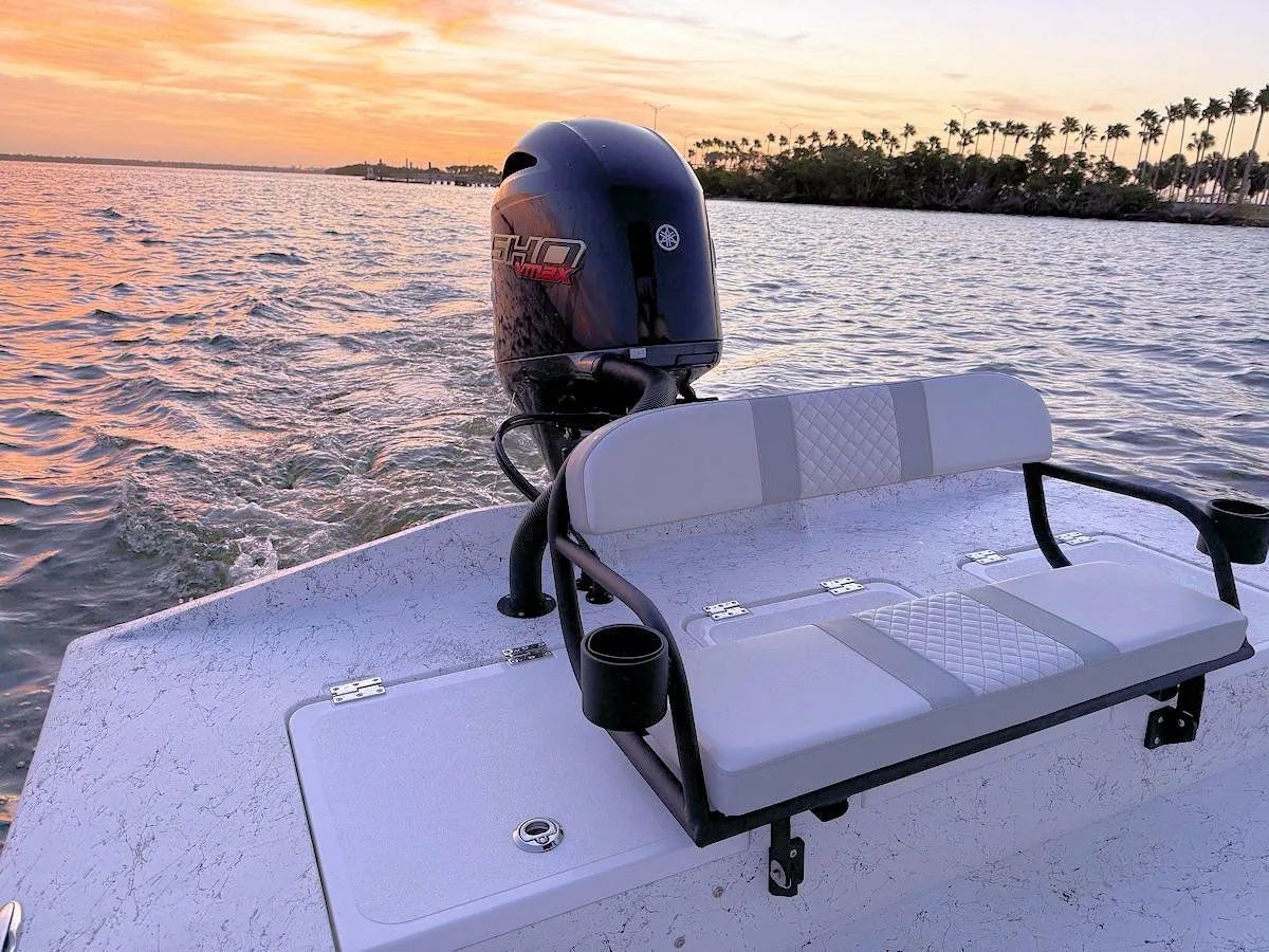 Small motorboat at sunset on calm water with an outboard motor and padded bench seat