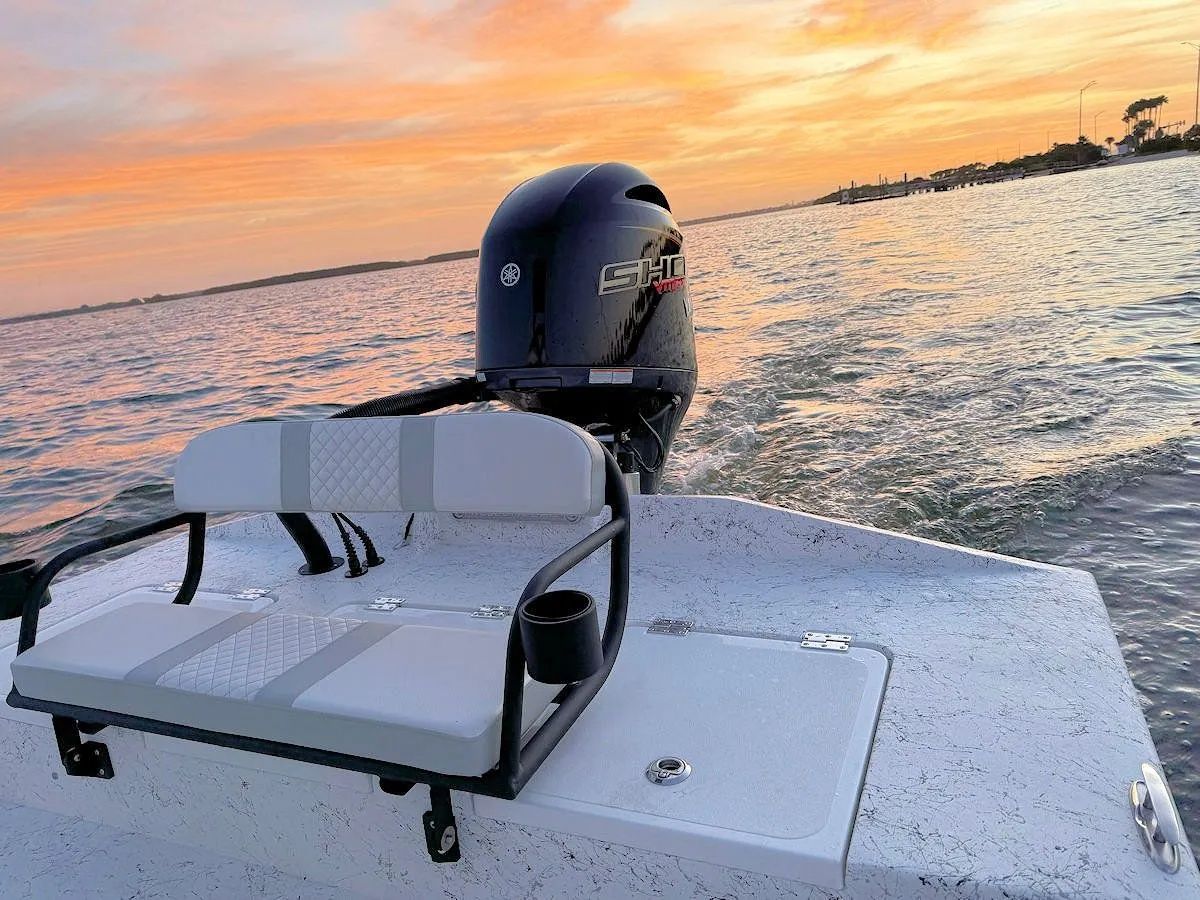 Boat stern with white seating and an outboard motor at sunset on calm water