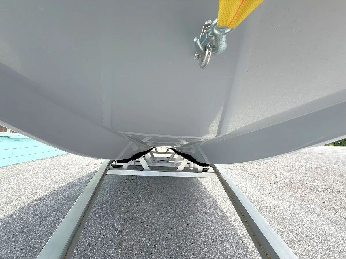 Close-up of a gray boat hull resting on a trailer, with a yellow strap at the bow.