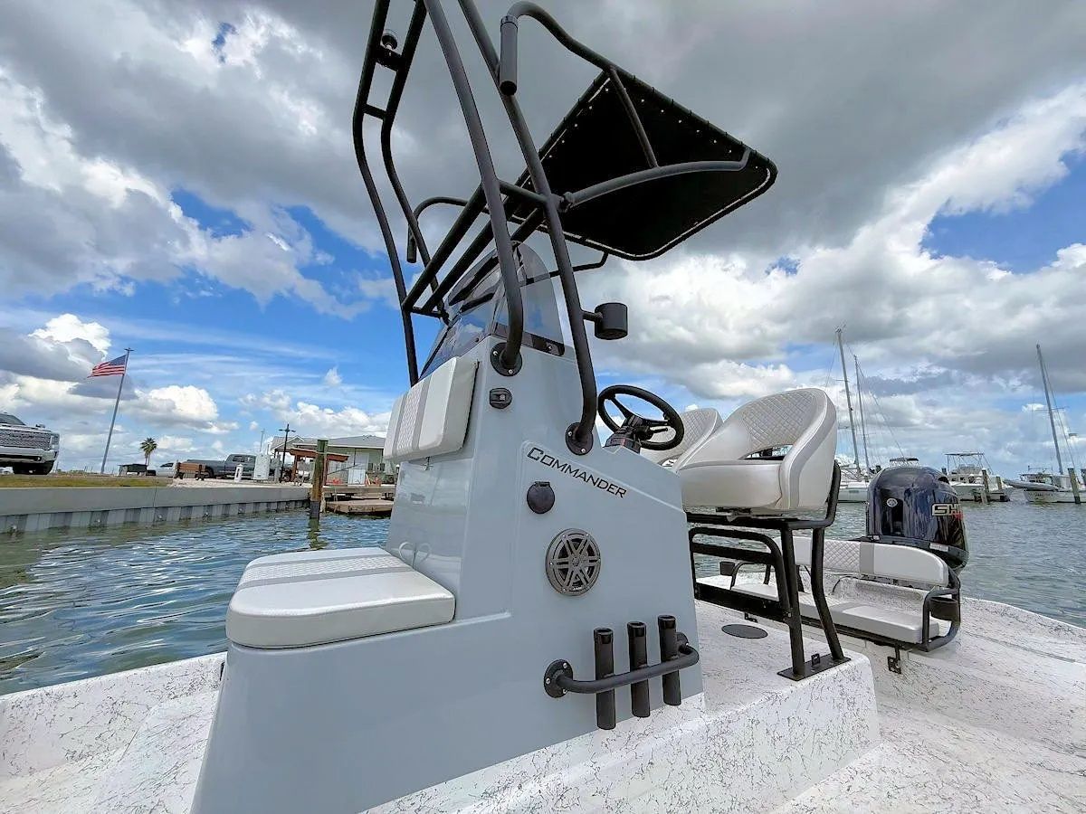 White center-console fishing boat at a marina with T-top canopy and calm water under a cloudy sky