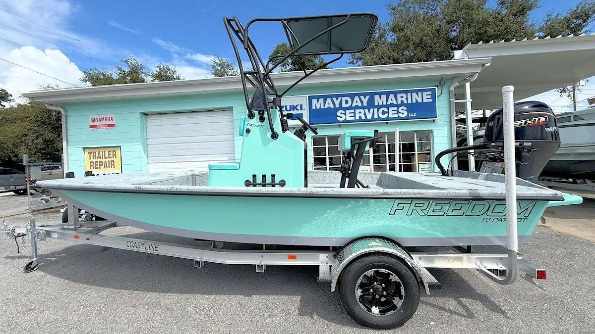 Light blue boat on trailer parked beside a marina service building with a Mayday Marine Services sign.