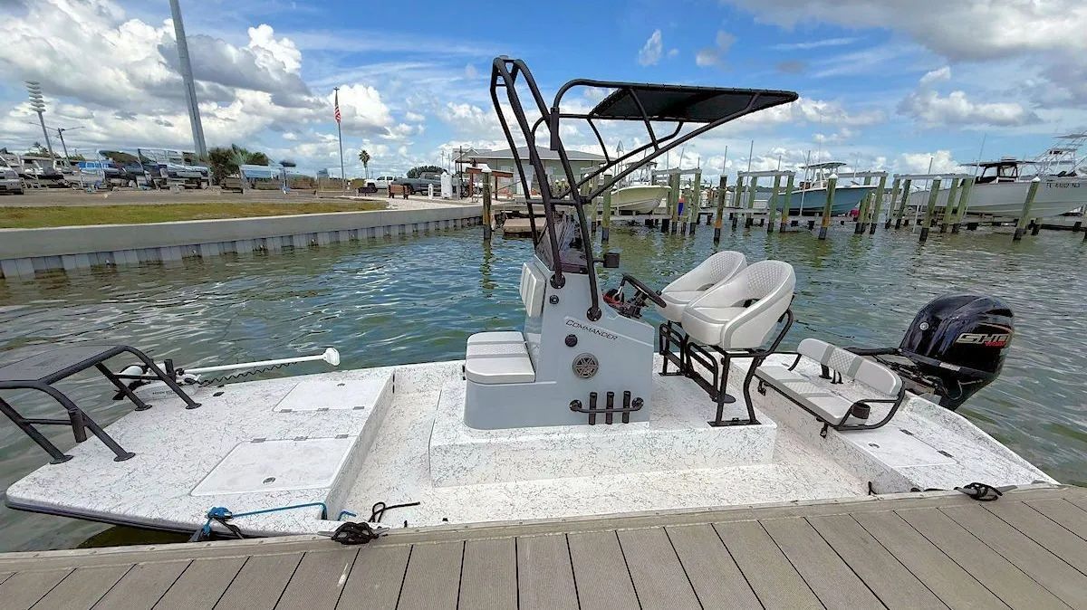 Docked fishing boat with outboard motor and raised canopy on a marina beside calm water.