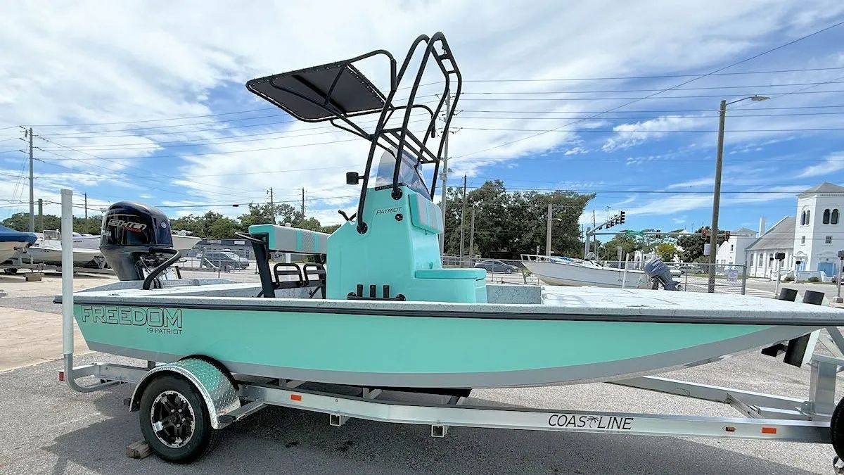 Turquoise center-console boat on a trailer at a marina, under a cloudy sky