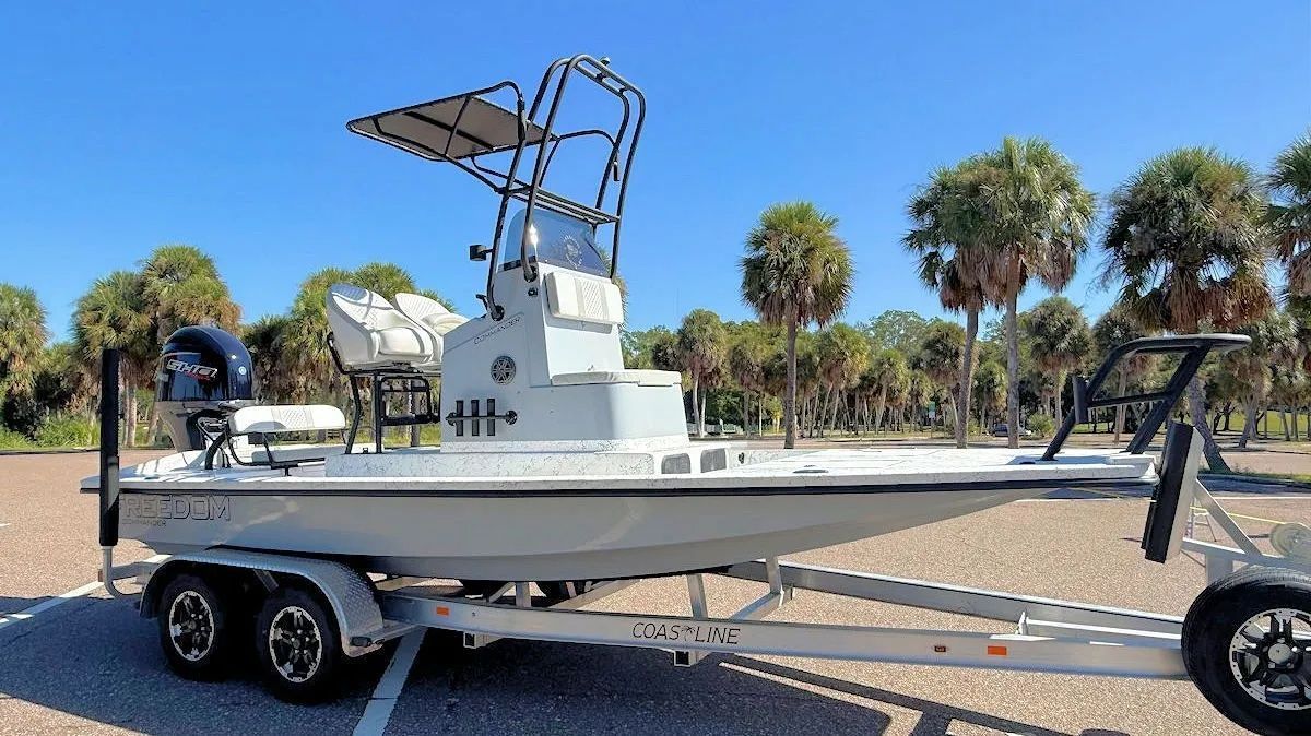 White center-console boat on a trailer parked outdoors under a clear blue sky.
