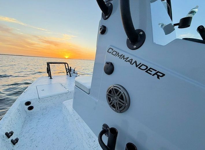 Fishing boat deck at sunset with calm ocean and orange sky, showing the word “COMMANDER” on the side