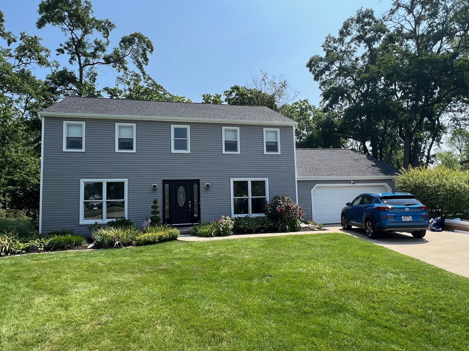 A blue car is parked in front of a gray house.