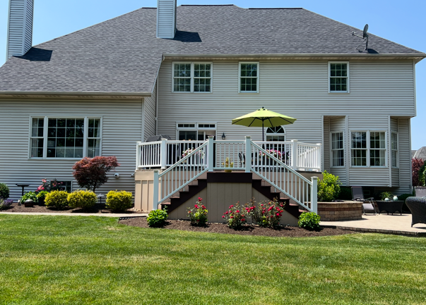 A large white house with a large deck and stairs leading up to it.
