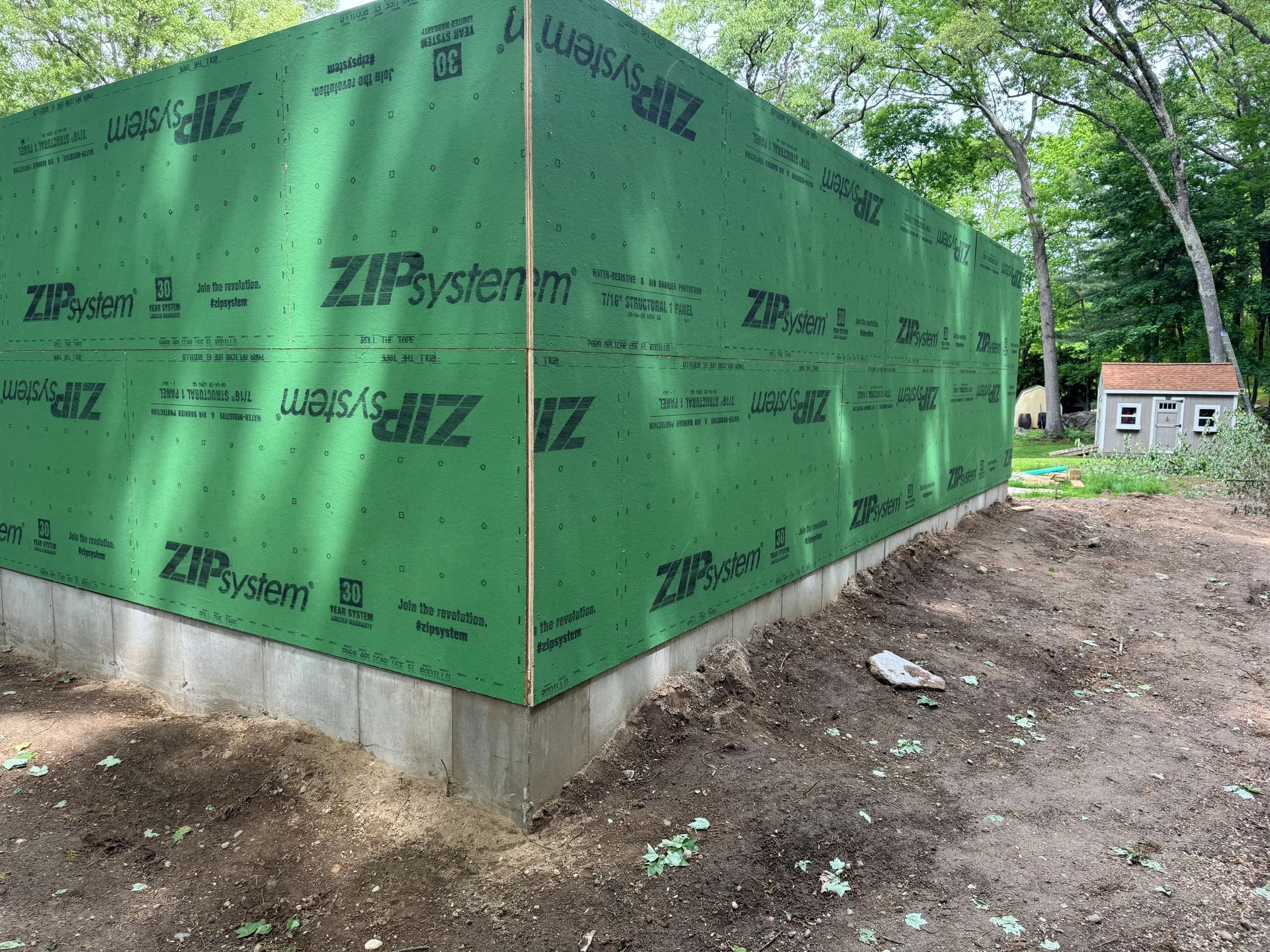 Green ZIP System house wrap on a small building foundation at a wooded construction site