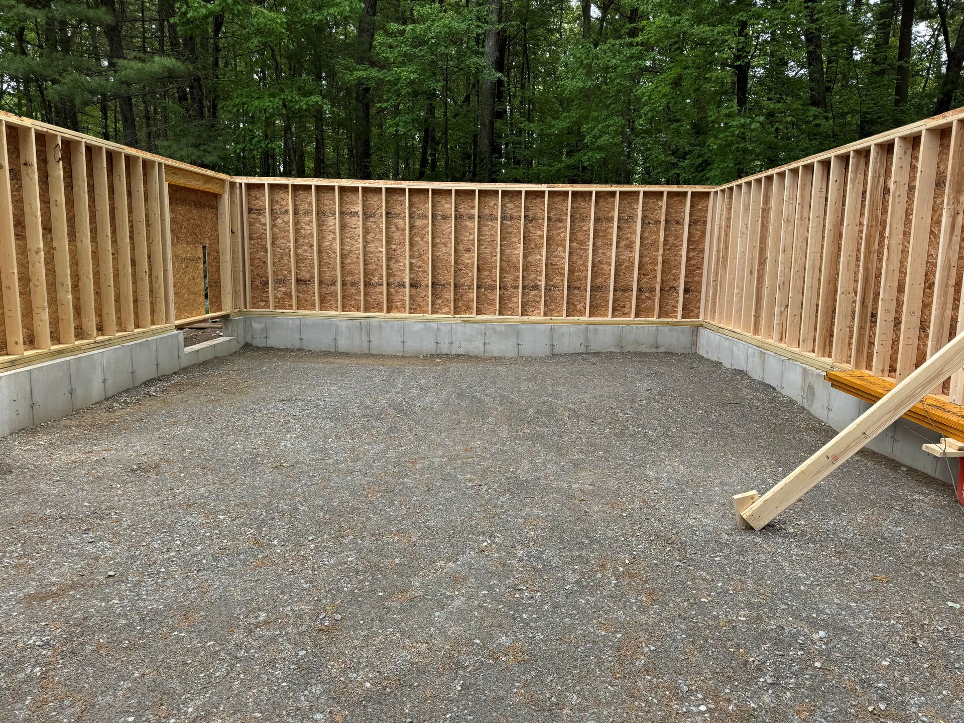 Empty gravel yard with wooden fence and concrete foundation walls in a wooded area