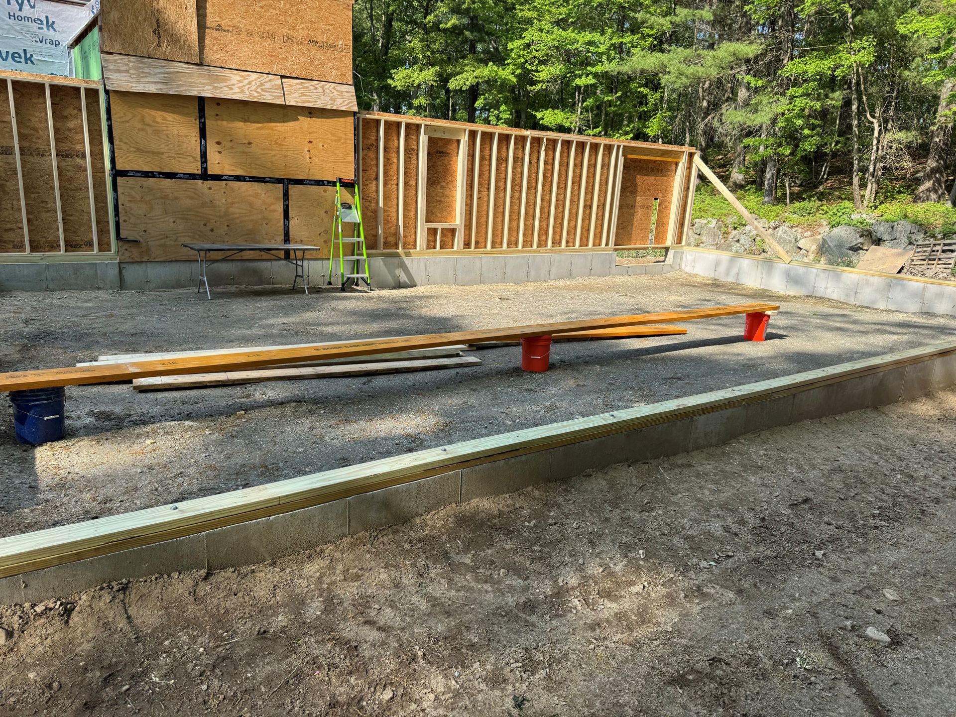 Construction site with gravel trench, wooden framing, and a plank resting on red supports.