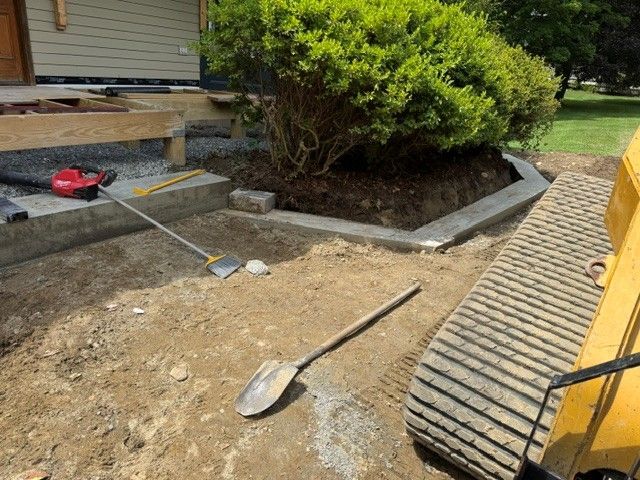 Construction scene with shovel and excavator track beside a house and shrub bed