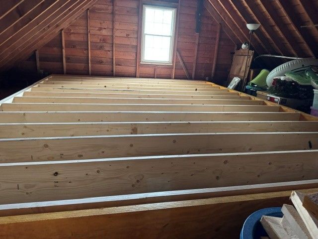 Wooden attic loft with exposed rafters and a skylight, covered by evenly spaced floor joists.