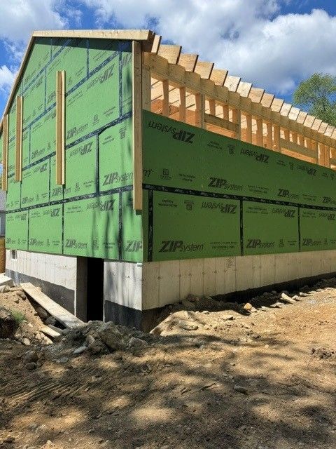Partially built house framed in wood, wrapped in green house sheathing on a dirt lot