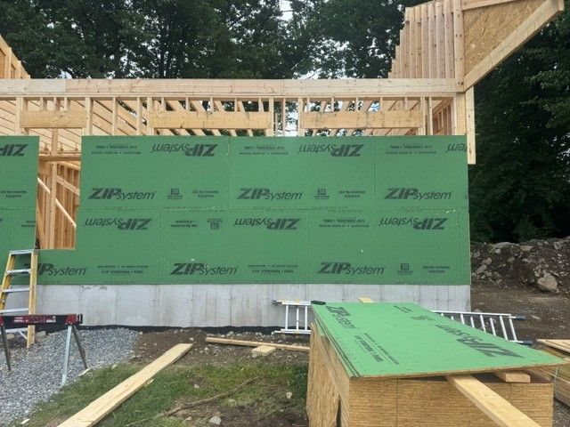 Partially built house with green ZIP sheathing, exposed wood framing, and ladders at the front