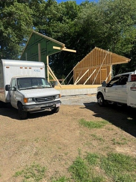 Two work vans parked beside a wooden pavilion under construction in a grassy lot