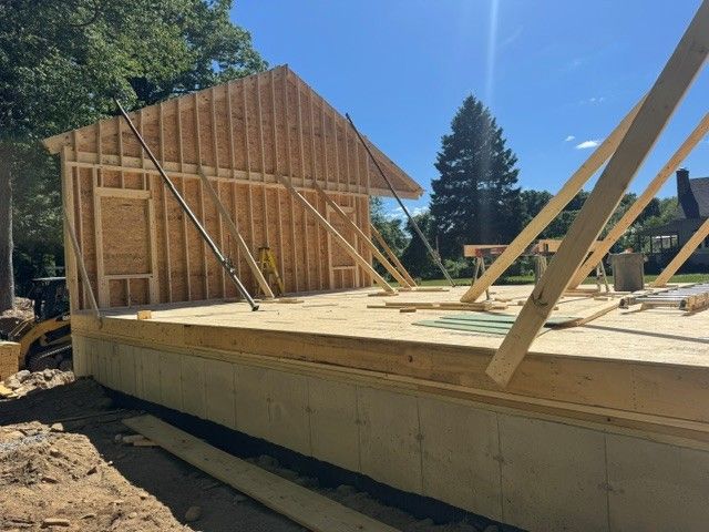 Partially built wooden house foundation with wall framing and roof trusses on a sunny construction site