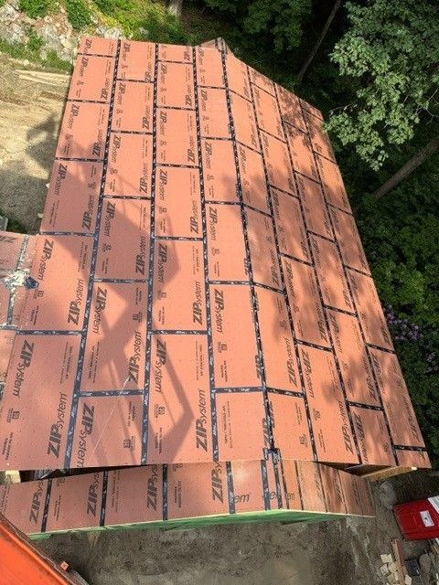 Orange roofing panels installed on a sloped roof beside dense green trees