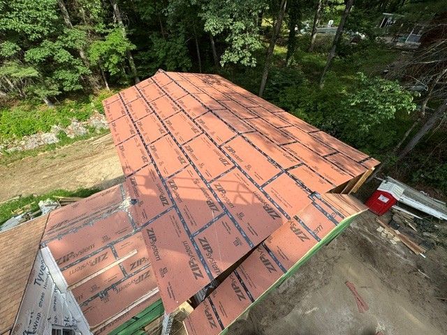 Partially installed copper-colored metal roof on a house surrounded by trees