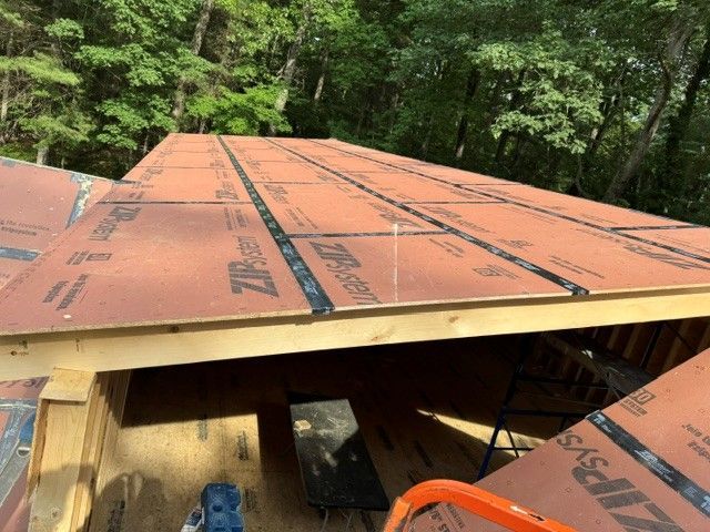 Partially covered roof with orange roofing panels on a wooden structure, surrounded by trees