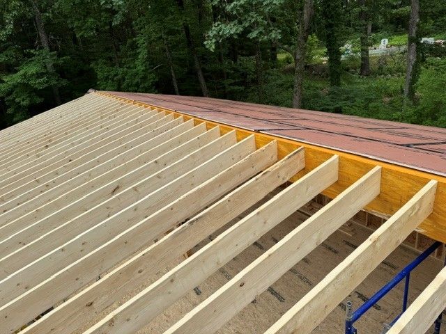Partially built wooden roof framing with plywood sheathing on one side and exposed rafters on the other