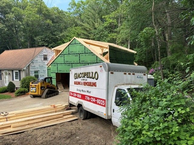 Construction trailer and dumpster beside a house under renovation, with lumber and green sheathing on the structure